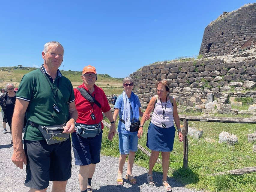 Vier Personen spazieren bei sonnigem Wetter an einer antiken Steinruine entlang.