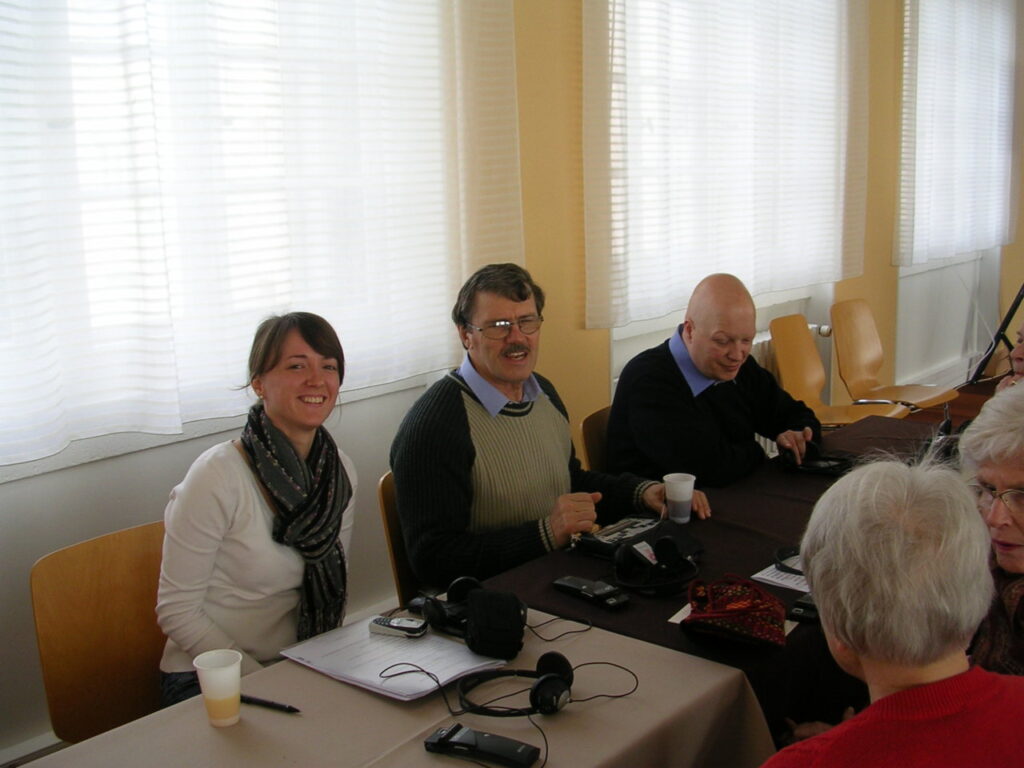 Eine Gruppe von Menschen sitzt an einem Tisch und unterhält sich in einem Raum mit großen Fenstern.