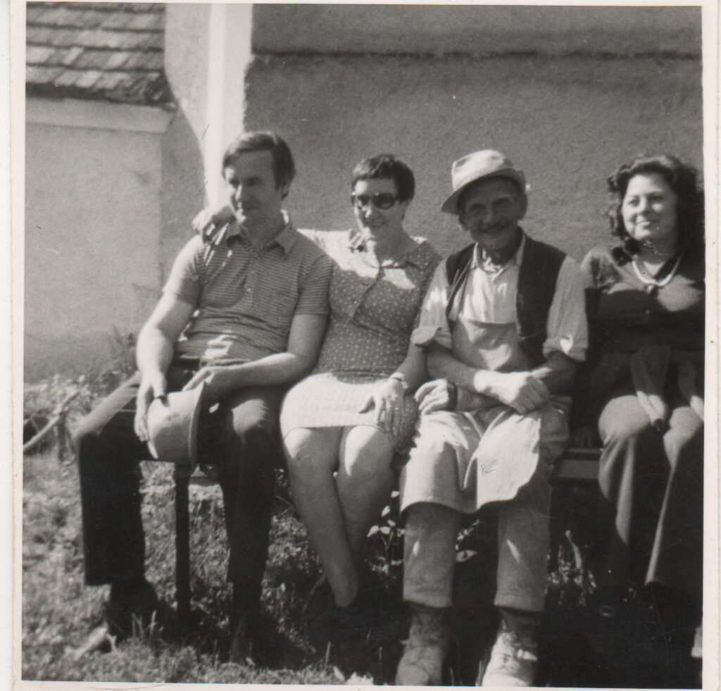 Eine Gruppe von vier Personen sitzt nebeneinander auf einer Bank im Freien und lächelt.