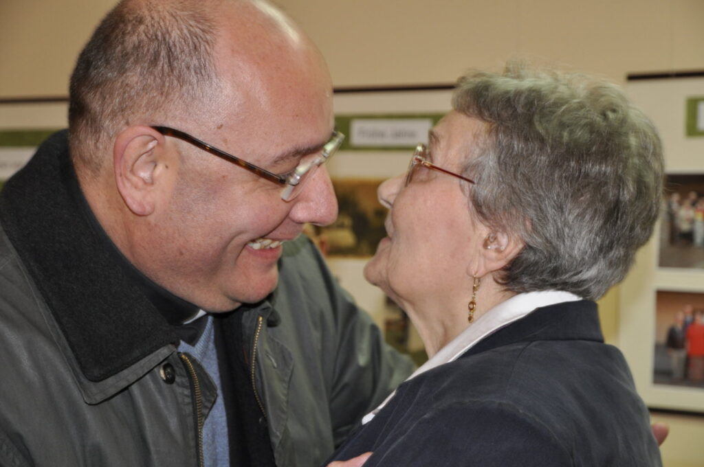 Ein Mann und eine ältere Frau lächeln sich herzlich an und umarmen sich.