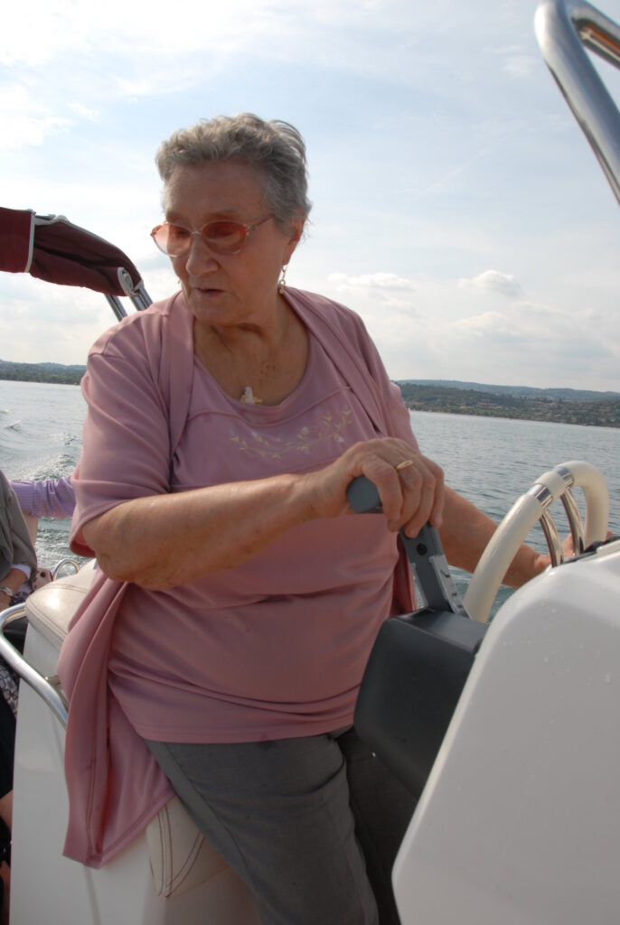 Eine ältere Frau in einer rosa Bluse steuert ein Boot auf einem See.