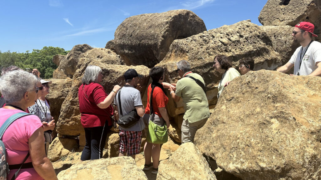 Eine Gruppe von Menschen erkundet im Freien zwischen großen Felsen eine archäologische Stätte.