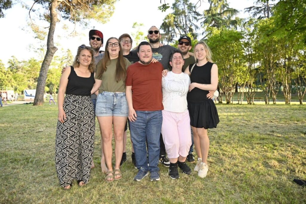 Eine Gruppe von zehn Menschen lächelt in einem parkähnlichen Garten in die Kamera, umgeben von Bäumen.