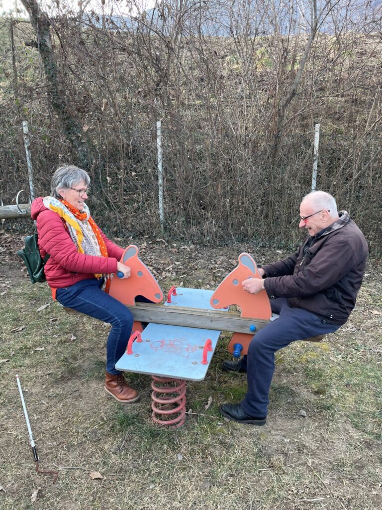 Zwei Menschen sitzen auf einem Wippspielgerät im Freien und lächeln sich an.