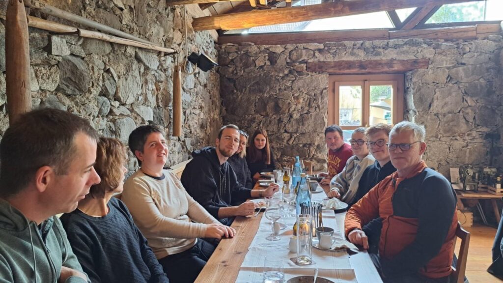 Eine Gruppe von Menschen sitzt in einer rustikalen Umgebung an einem langen Holztisch beim Essen.