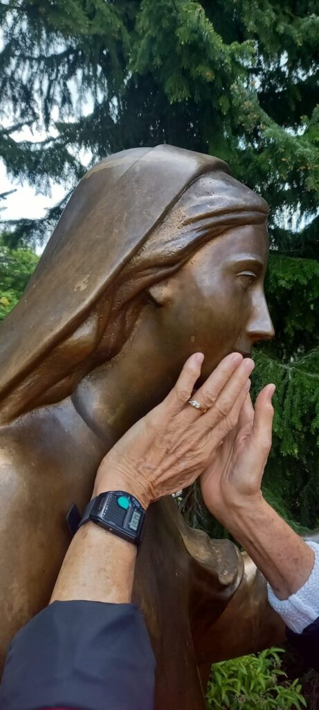 Eine Person tastet mit den Händen das Gesicht einer Bronzestatue, um die Struktur zu erfühlen.