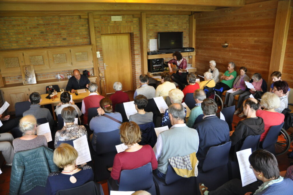 Eine Gruppe von Menschen sitzt in einem Raum und hört einer Person zu, die vorne spricht.