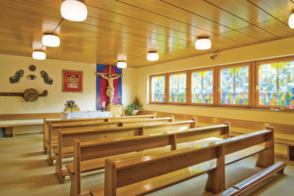 Eine kleine Kapelle mit Holzbänken, einem Altar und bunten Glasfenstern.