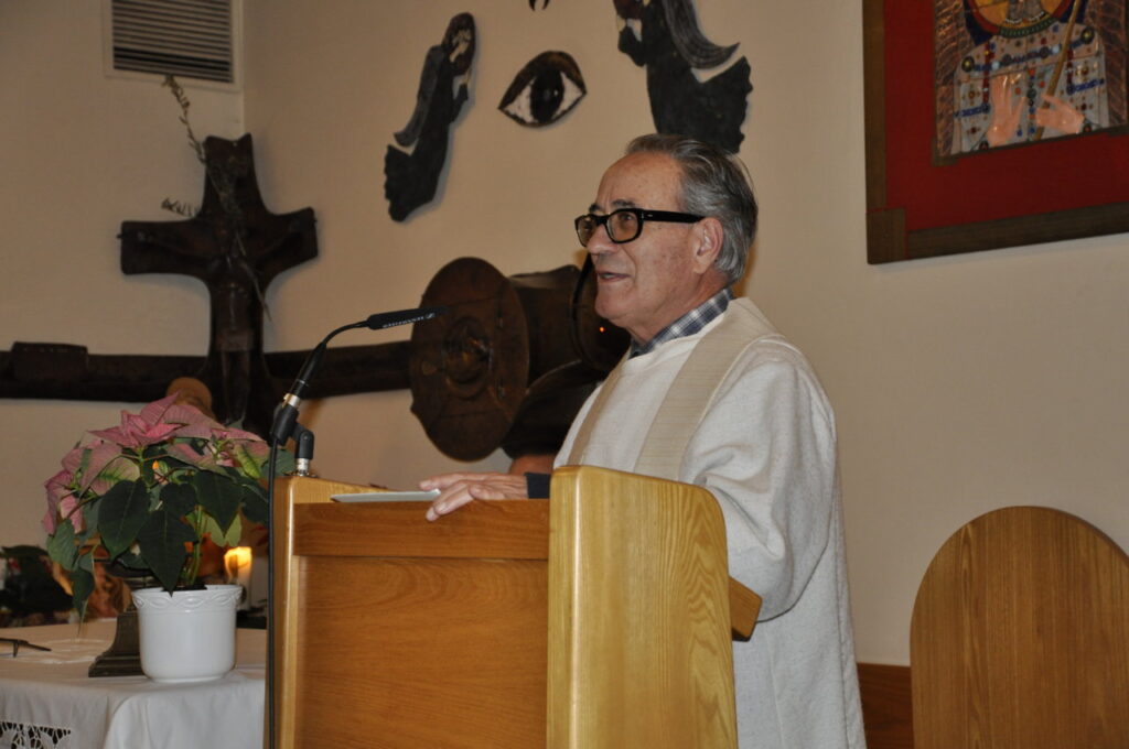 Ein älterer Mann hält eine Rede an einem Holzpult in einem geschmückten Raum.