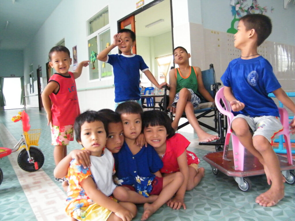 Eine Gruppe von Kindern unterschiedlicher Altersgruppen sitzt und steht in einem hellen Raum auf einem gemusterten Boden.