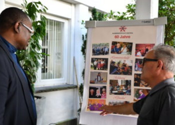 Zwei Männer betrachten gemeinsam eine Pinnwand mit Fotos zur Feier von 60 Jahren.