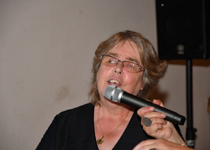 Eine Person mit Brille hält ein Mikrofon und singt oder spricht in ein Mikrofon.