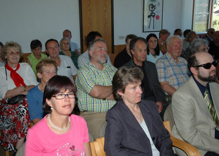 Eine Gruppe von Menschen sitzt aufmerksam in einem Raum, während einer davon eine Sonnenbrille trägt.