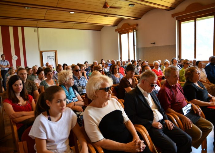 Eine große Gruppe von Menschen sitzt in einem Veranstaltungsraum und lauscht aufmerksam.