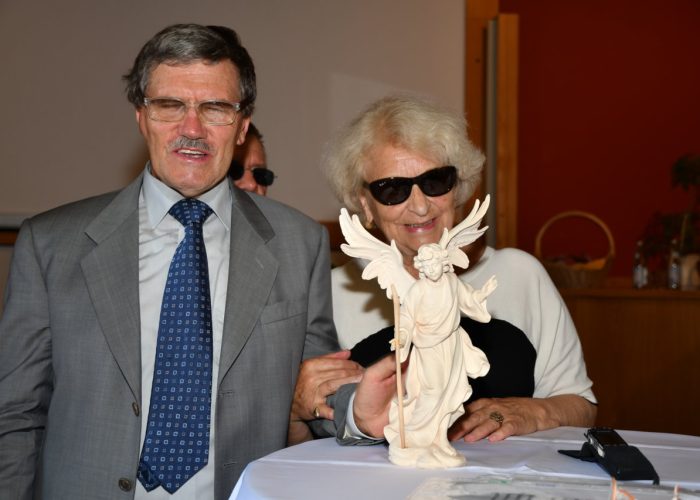 Ein Mann und eine Frau stehen lächelnd hinter einer Engelsstatue auf einem Tisch.