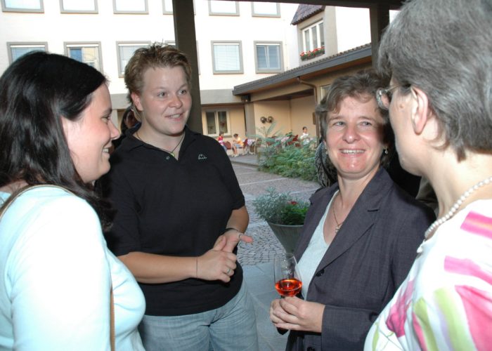 Vier Personen stehen lächelnd in einem Hof und unterhalten sich miteinander.