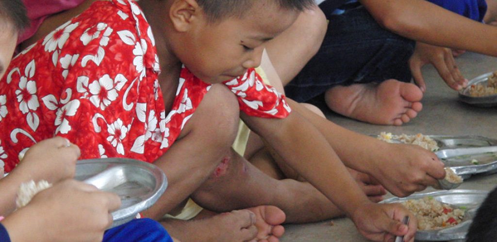 Kinder sitzen auf dem Boden und essen gemeinsam Reis von Metalltellern.