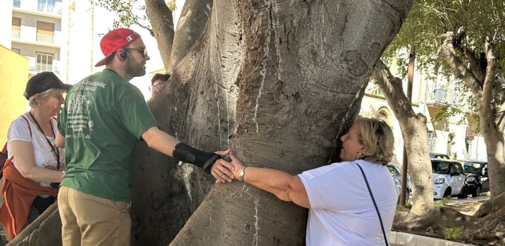 Mehrere Personen umarmen gemeinsam einen großen Baumstamm in einer städtischen Umgebung.